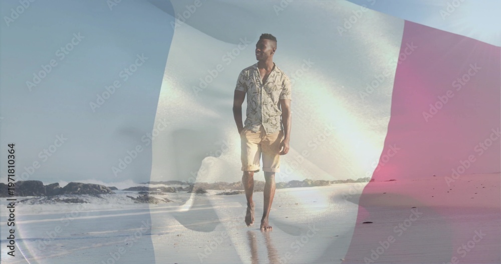 Obraz premium Walking man in patterned short-sleeve shirt, shorts on wet sand, with faint tricolor flag overlay
