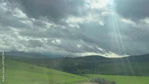 A serene video showcasing a green mountain landscape under a cloudy sky with sun rays