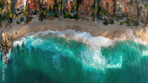 Aerial perspective captures azure ocean waves crashing onto a sandy shore adjacent to upscale coastal residences.