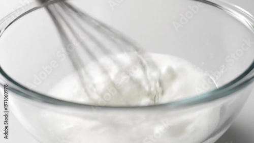 Whisking egg whites in a glass bowl to create a fluffy white foam for baking or cooking.