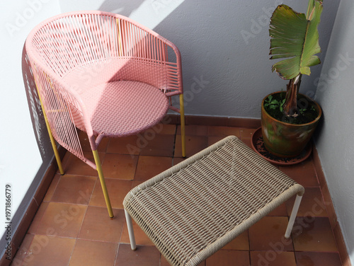 Small balcony corner with pink chair, footstool and potted plant near wall. Cozy outdoor seating for relaxation, home interior extension, quiet rest and simple lifestyle space.