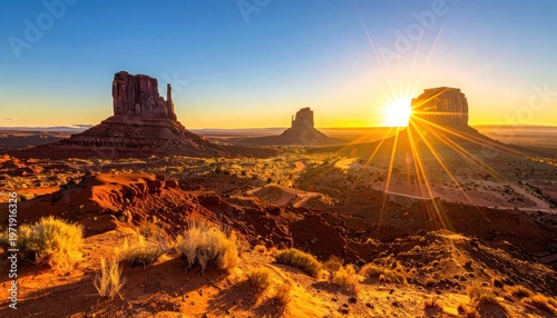 A breathtaking sunset illuminates the iconic sandstone buttes of Monument Valley, casting a warm golden glow across the vast desert landscape.