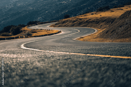 Low angle view of winding asphalt road with white lane marking illuminated by warm sunset light, detailed textured surface and dramatic curve through countryside landscape
