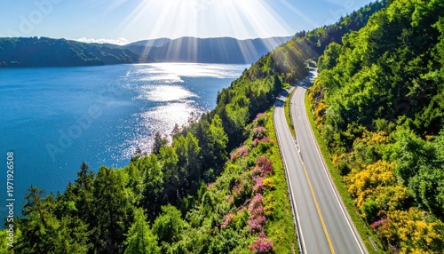 scenic winding coastal road along deep blue lake with sunlight flare and lush green forest, road trip and travel vacation summer atmosphere