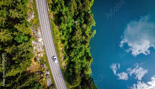 Aerial drone view of a car driving along a scenic coastal road next to dense green forest and deep blue lake water, travel adventure
