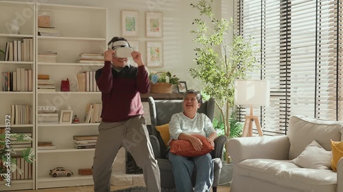 Senior Asian couple enjoying VR game experience in living room, elderly man and woman smiling while using virtual reality headset, fun technology activity, active lifestyle, modern entertainment at ho