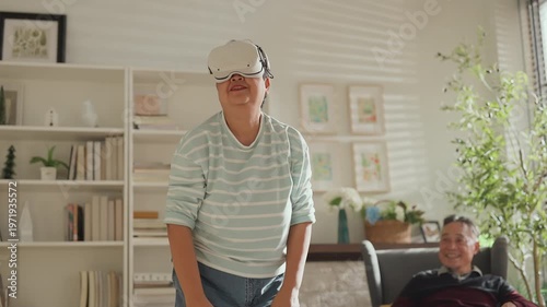 Senior Asian couple enjoying VR game experience in living room, elderly man and woman smiling while using virtual reality headset, fun technology activity, active lifestyle, modern entertainment at ho