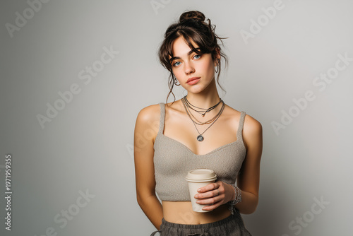 Young woman in modern streetwear holding coffee cup in studio.