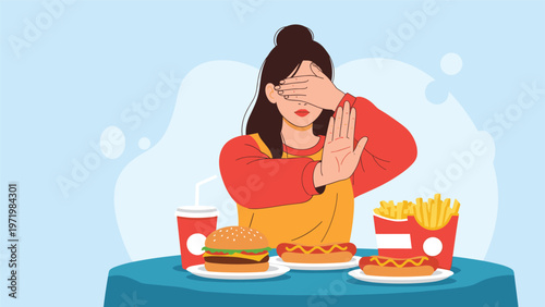 Young woman sitting at a table and covering her eyes while gesturing stop to unhealthy fast food like burgers, hot dogs, and fries.