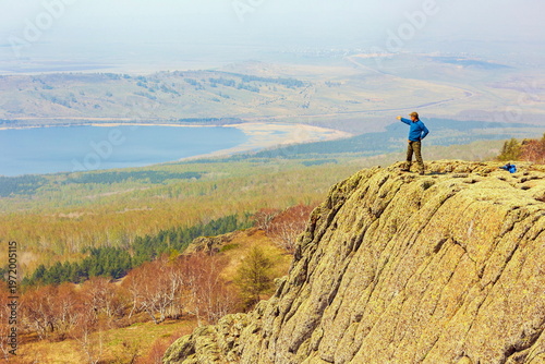 an elderly happy tourist stands on a high rock against the backdrop of the Ural mountains on a summer day