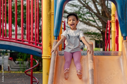 Fotografía A happy little Asian girl sliding down a slide at an outdoor playground