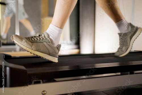 Close up of man's legs running on a treadmill in a gym. Low angle view of a person in sneakers jogging on a treadmill. Cardio workout session in a fitness club or home gym