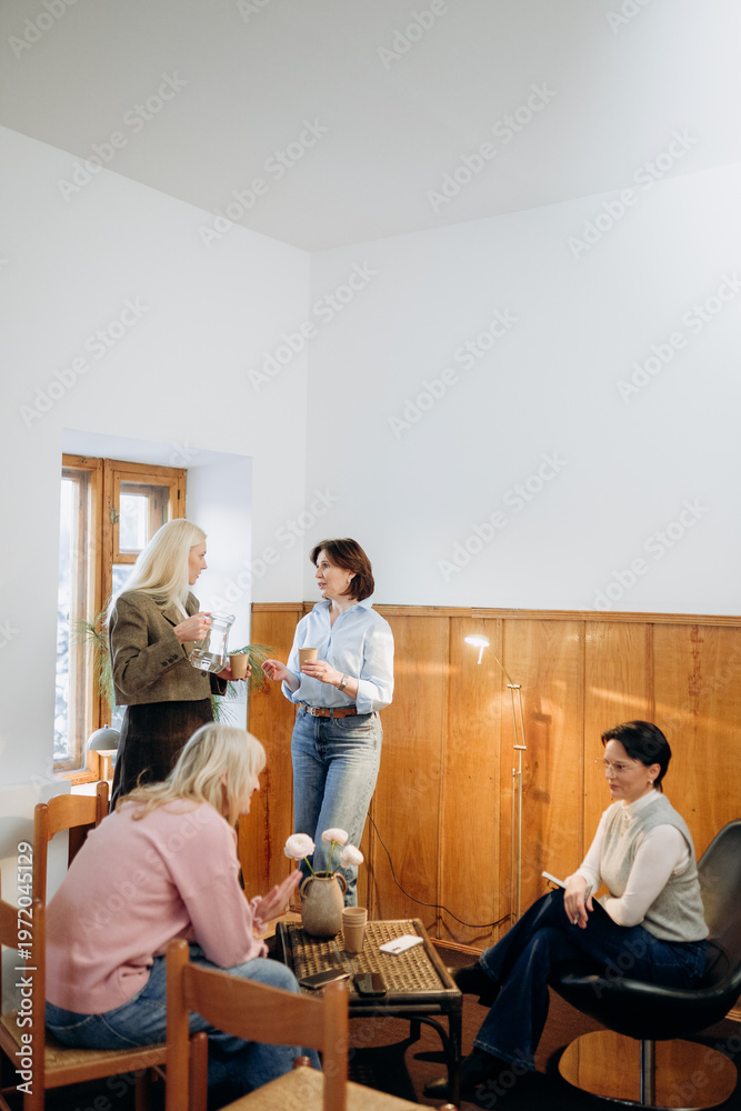 Fototapeta premium Three women engage in lively conversation while seated in a bright, inviting café. Natural light pours in, creating a warm atmosphere perfect for connection and joy.