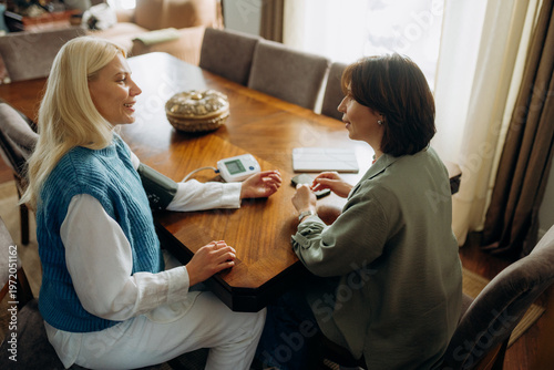 Obraz na plátně Two women engage in a friendly health consultation at a wooden dining table filled with warmth and natural light