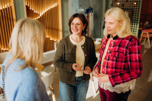 Billede på lærred In a warm cafe setting, three women share joyful conversations, exchanging smiles and laughter over coffee