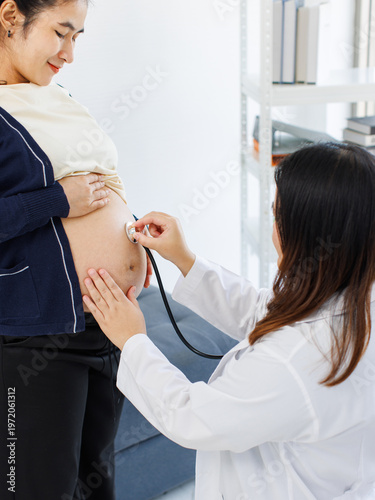 Asian happy young pregnant woman sit checkup female doctor with stethoscope in maternity hospital listening baby heartbeat in tummy last stages of pregnancy healthcare prenatal focus expecting mother.