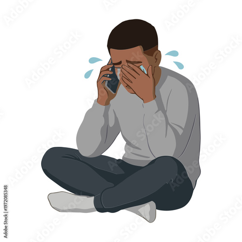 A man sits on the floor crying while talking on his phone with sadness.