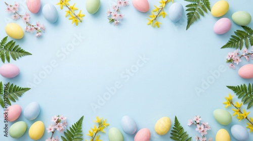 Flat lay of pastel Easter eggs, fern leaves, and spring flowers arranged as decorative border on light blue background. Festive seasonal composition with empty center space
