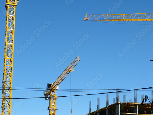 Three yellow construction cranes and a building under construction against a clear blue sky