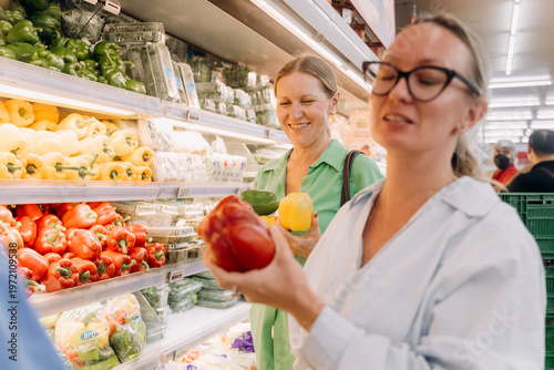 Fotografía Two women are looking at vegetables in a grocery store