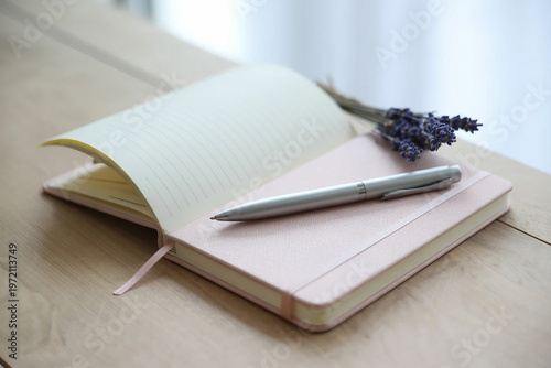 Pink and white striped notebook with a matching pen on a wooden desk by a sunny window.