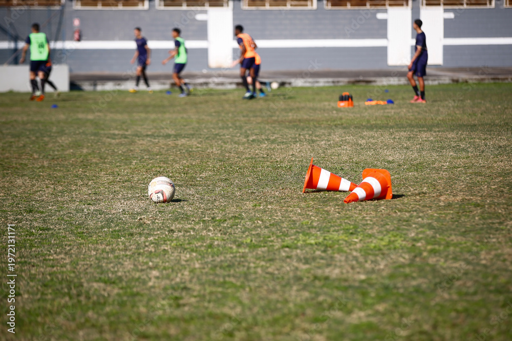 Obraz premium Training football equipments in a green grass football field while athletes practice during a sunny day 