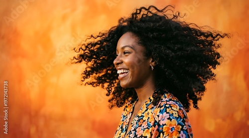 Joyful Black Woman with Voluminous Curly Hair Smiling Against Orange Wall.
