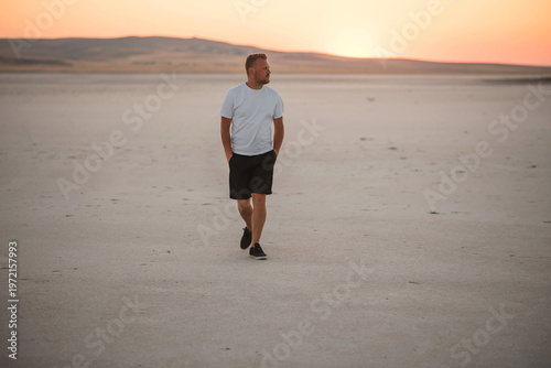 Foto Man walking alone in a vast, dry landscape during a beautiful sunset