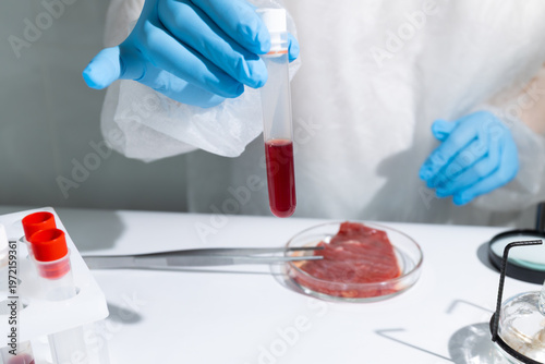 Bild auf Leinwand Woman scientist holding test tube with blood sample near lab-grown meat in petri dish