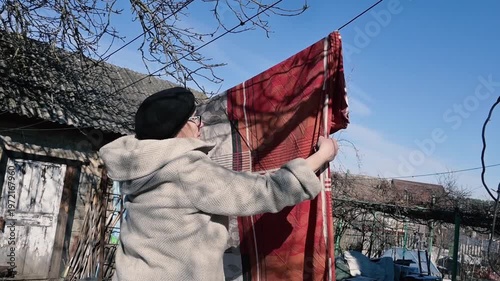 Elderly Woman Taking Down Laundry on Clothesline in Sunny Rural Yard