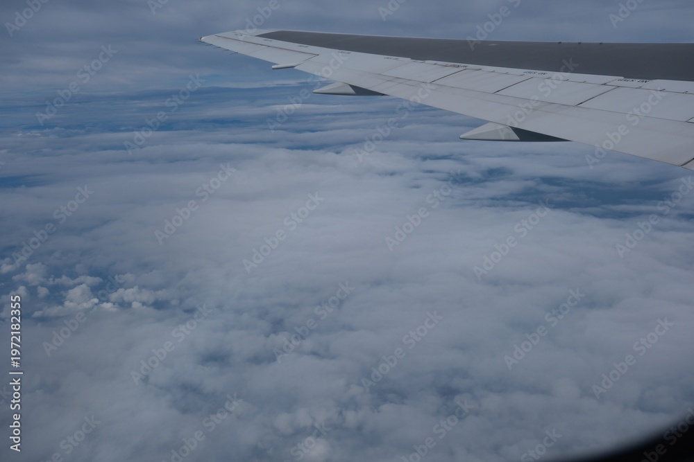 Obraz premium Airplane wing soaring above fluffy clouds in blue sky.