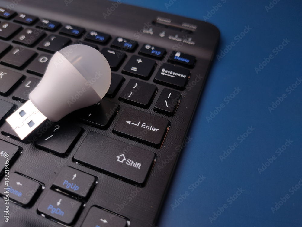 Obraz premium A close-up, top-down studio shot featuring a small white USB LED light bulb resting on a black laptop keyboard