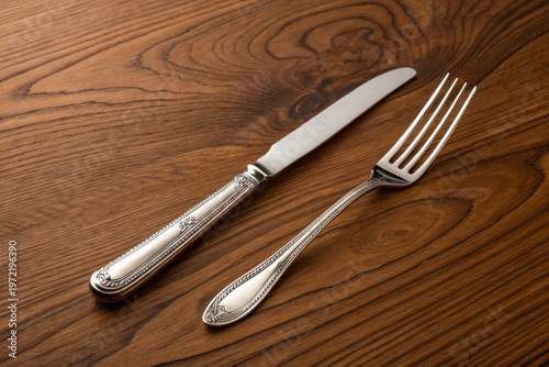Polished knife and fork with decorative handles lie neatly on wooden table with rich grain pattern