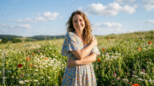 Young woman embracing herself in blooming wildflower field under sunny sky, serene summer lifestyle portrait