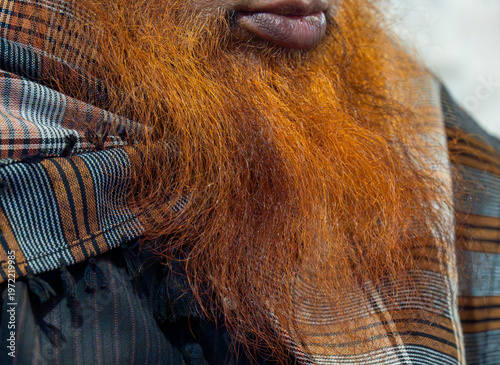 Close-up of a man’s henna-dyed beard with a traditional patterned scarf draped around his shoulders