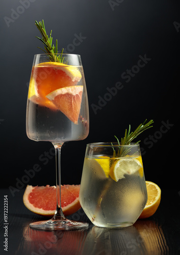 Gin tonic with ice, rosemary, lemon, and grapefruit on a black wooden table.