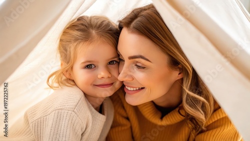 Mother Day Mother and daughter smiling warmly while lying together under a cozy blanket.