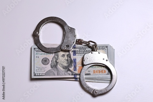 Close-up of handcuffs locking a bundle of US dollar bills, representing frozen assets, debt crisis, legal enforcement, and financial penalties. Concept of restricted funds, seized money, tax issues