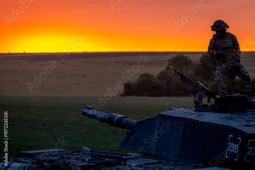 SALISBURY PLAIN, UK - JULY 29, 2025: A British Army Challenger 2 Main Battle Tank silhouetted at sunrise during a military exercise. The tank commander is visible standing in the turret.