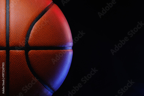 Basketball ball resting against dark background, showing its distinctive pebbled texture and black seams, with vibrant red and blue studio lighting
