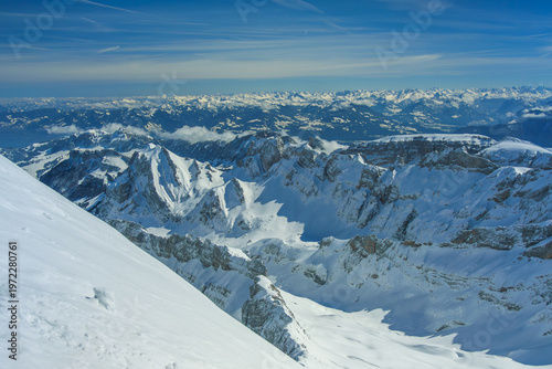 Snow covered mountain peaks under clear blue sky create breathtaking winter landscape. vast expanse of snow and distant mountain ranges evoke sense of tranquility and awe