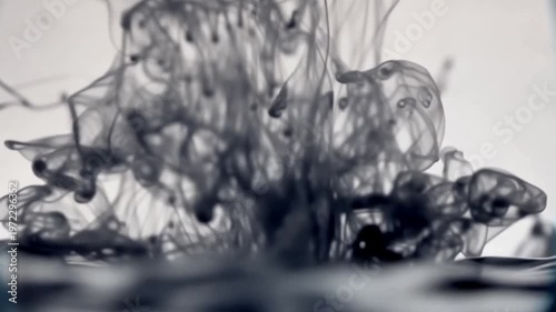 Macro shot of black ink diffusing in clear water against a white background, featuring intricate plumes, wispy smoke-like swirls, and organic fluid motion patterns.