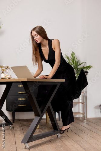 Woman working on laptop while standing at a desk in a stylish office in the daytime