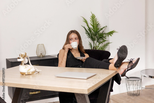 Woman drinking coffee while relaxing in modern office setting with stylish decor and casual posture