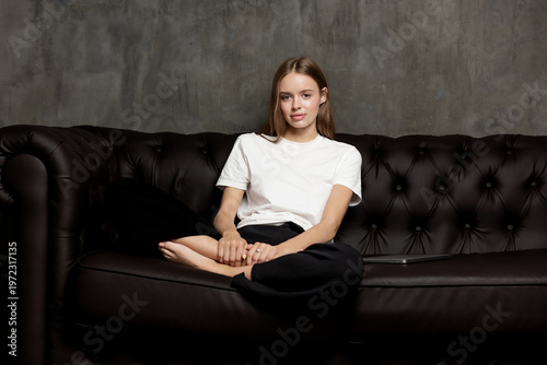 Young woman relaxing on black leather couch in indoor setting with neutral background