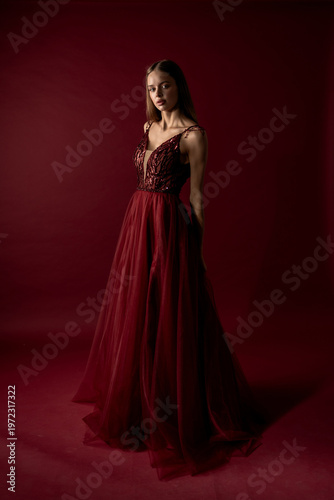 Model poses in a red dress with a dark background for a fashion shoot
