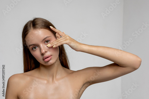Model poses while showcasing beauty with hand against face in a minimal studio setting