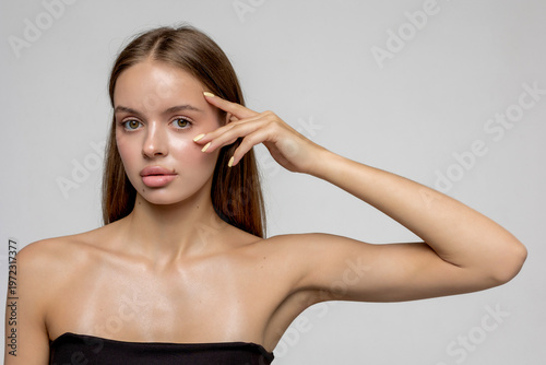 Model poses with hand on face against plain background in studio setting