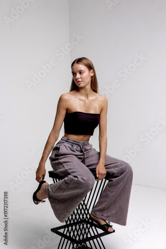Model poses on a black geometric chair in a bright studio space during a fashion shoot