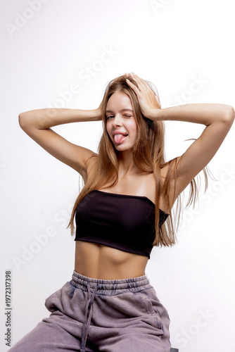 Young woman poses playfully with hands on her head and sticks her tongue out in studio setting